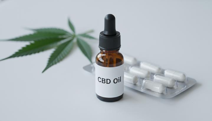 Эффективность каннабиса для снятия хронической боли оказалась ограниченной Медицинские продукты на основе каннабиса: флакон с маслом и пипеткой, капсулы и лист каннабиса на белом столе в лаборатории.