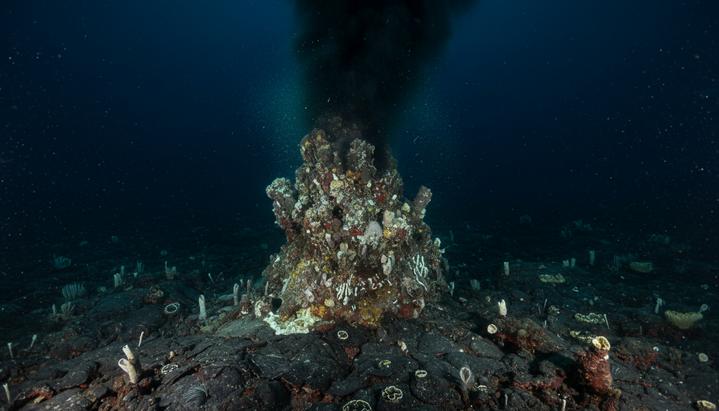 Подводный гидротермальный источник «черный курильщик» извергает темный поток минералов в глубине океана.