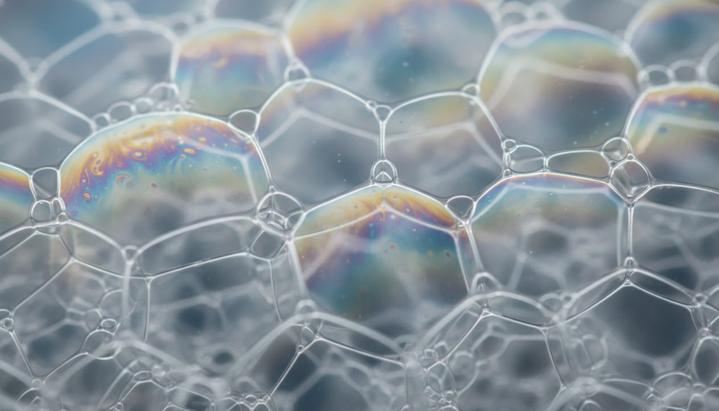 Физика пены подчиняется тем же законам, что и искусственный интеллект Крупный план влажной пены, где множество прозрачных пузырьков разного размера образуют сложную ячеистую структуру.